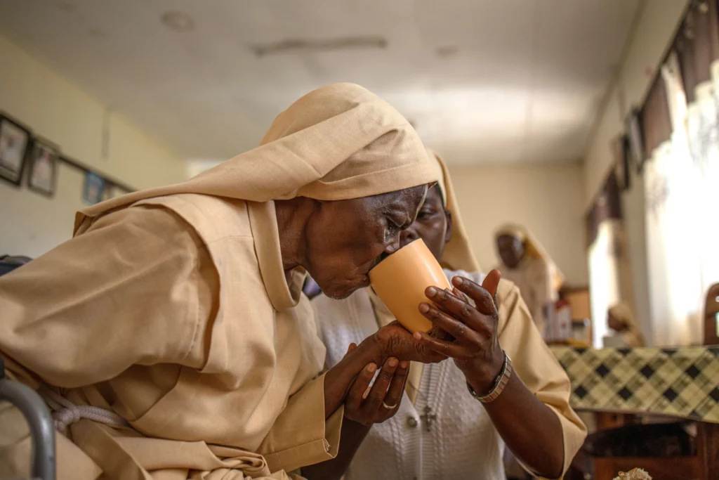 Sister Mary Consolata Nakawoojwa assists an elderly nun as she takes tea at the Little Sisters of St Francis premises in Nkokonjeru Uganda Stuart Tibaweswa for NPR